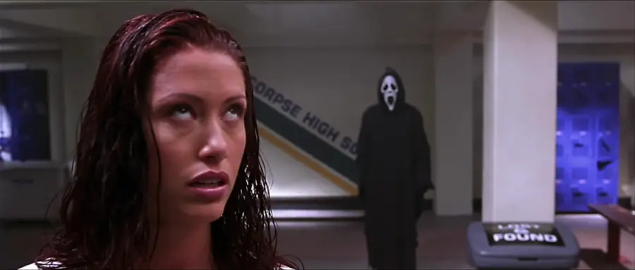 A woman with wet hair looks upward in a school hallway while a masked figure in a black robe stands menacingly in the background near lockers and a lost and found bin.