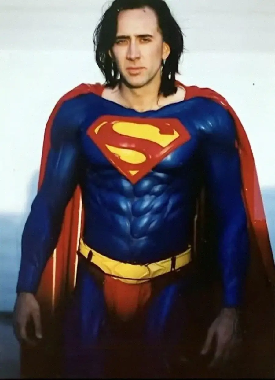 A person with long dark hair is wearing a classic Superman costume with a red cape, blue suit, and yellow belt, standing and looking at the camera.