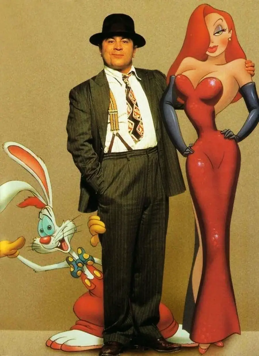 A man in a pinstripe suit and hat stands between Roger Rabbit, a cartoon rabbit, and Jessica Rabbit, a glamorous cartoon woman in a red dress, both characters from "Who Framed Roger Rabbit.