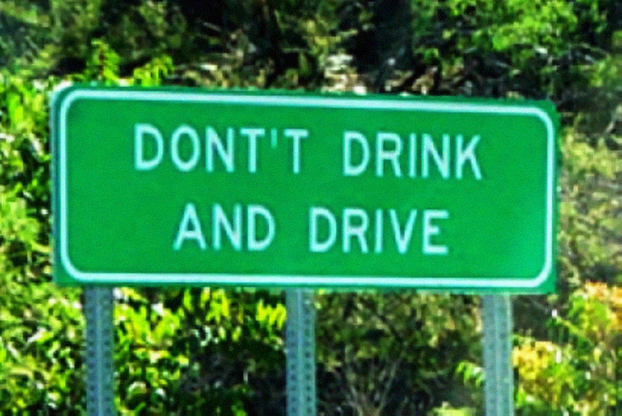 A green road sign with white text that reads "DON'T DRINK AND DRIVE," set against a background of trees and greenery.