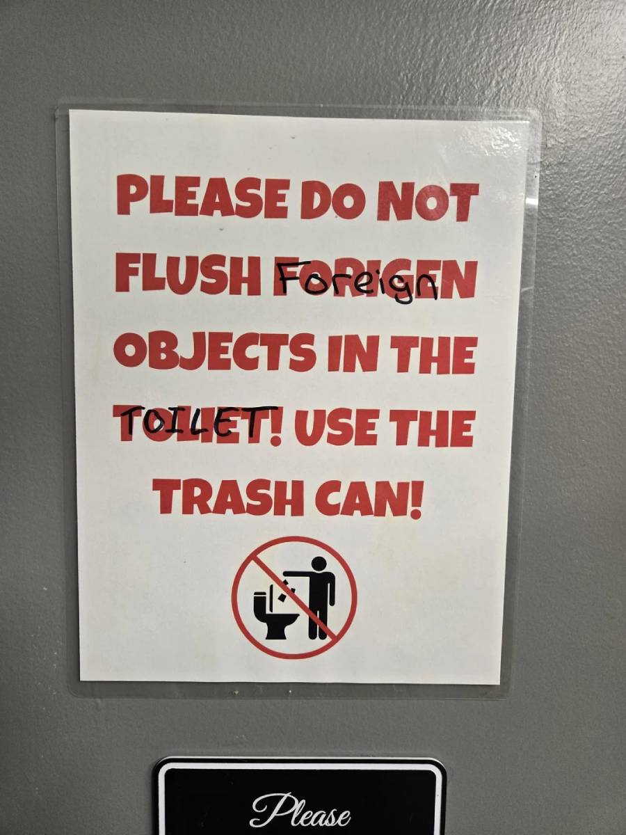A sign reads: “PLEASE DO NOT FLUSH OBJECTS IN THE TOILET! USE THE TRASH CAN!” with the words “Foreign” and “TOILET” scribbled out. Below is a no-flushing symbol with a person and a toilet.