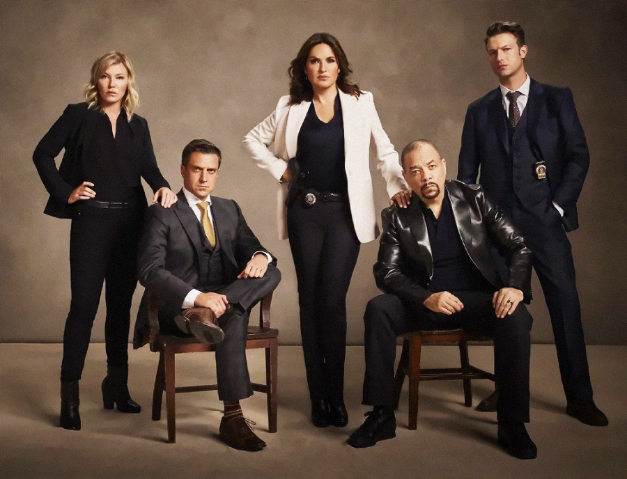 Five people in formal and business attire pose for a photo against a neutral background; three are standing, two are seated, and all look directly at the camera with serious expressions.