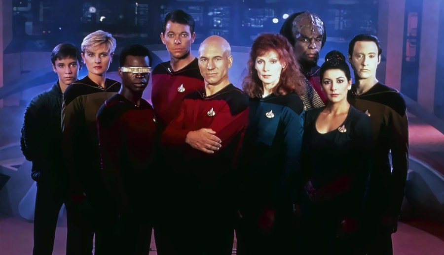 Nine people in Starfleet uniforms stand together on a futuristic spaceship bridge, posing for a group photo. The background features sci-fi equipment and dim lighting, giving a high-tech atmosphere.