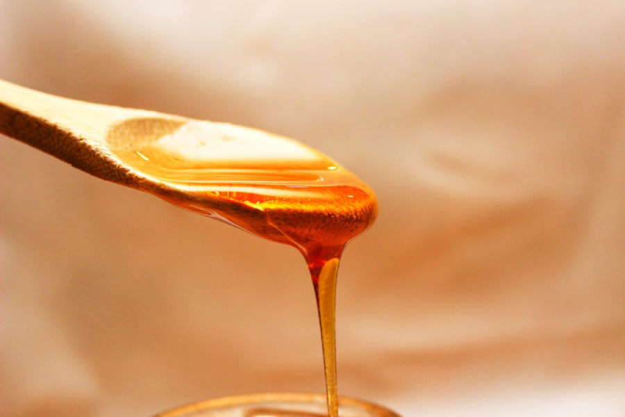 A wooden spoon with golden honey dripping off the edge against a soft, blurred background.