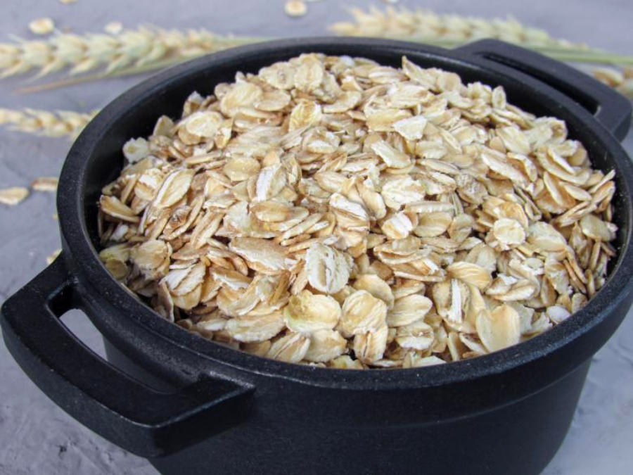 A black pot filled with uncooked rolled oats, with some oats scattered in the background on a gray surface.