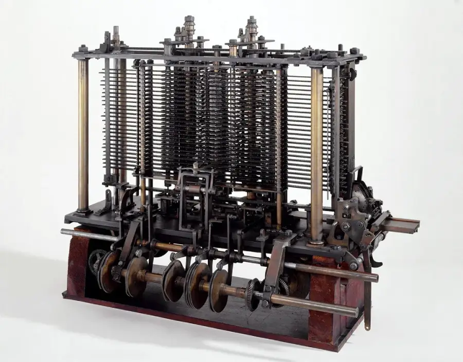A mechanical device with multiple vertical gears and rods, metal frames, and rotating shafts, resembling an early calculating machine or computer, displayed on a flat surface against a plain background.
