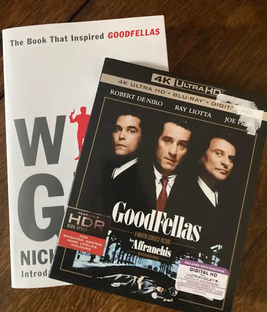 A copy of the book "Wiseguy" by Nicholas Pileggi is partially covered by a 4K Ultra HD Blu-ray case of the film "Goodfellas," featuring Robert De Niro, Ray Liotta, and Joe Pesci on the cover.