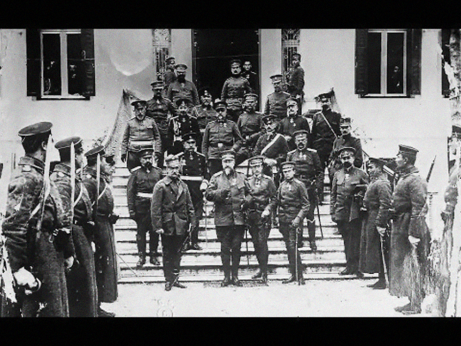 A black-and-white historical photo shows a large group of military officers in uniform posing on the steps of a building, with several men standing and some sitting in rows.