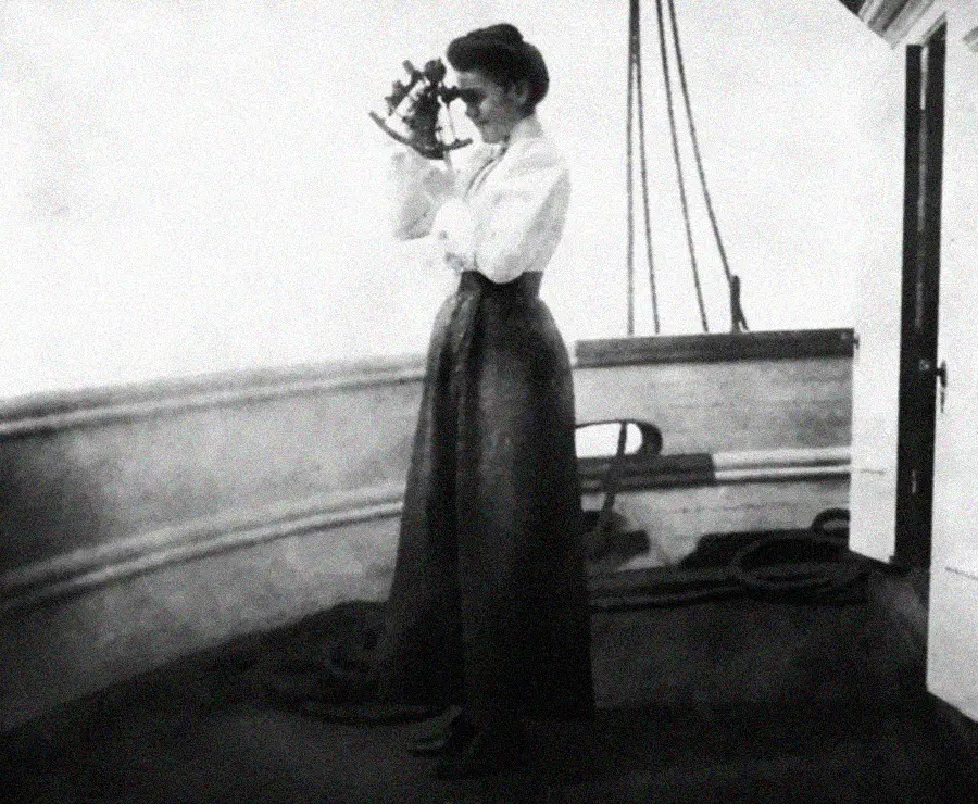 A woman in early 20th-century clothing stands on a ship’s deck using a sextant to navigate, with ship railings and ropes visible in the background.