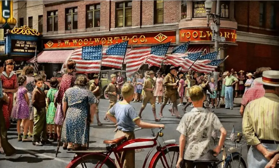 A vintage street scene shows a parade with Boy Scouts carrying American flags, while a crowd of men, women, and children watch in front of a Woolworth store. Bicycles and people in 1940s clothing are visible.
