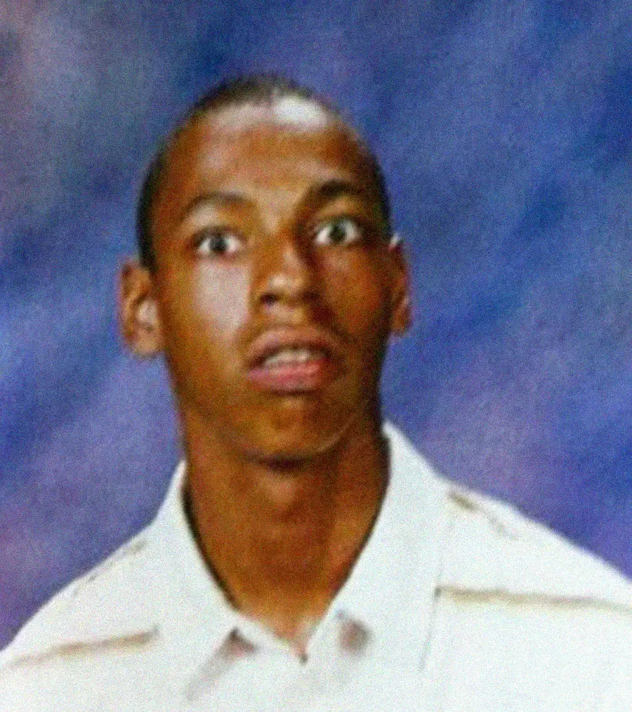A young man with short hair and wide eyes is staring ahead with a surprised expression, wearing a light-colored collared shirt, in front of a blue and purple mottled background.