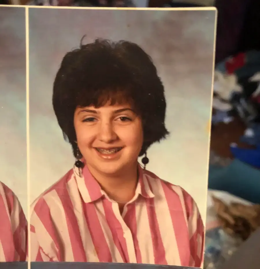 A school portrait of a smiling young person with short dark hair, wearing a pink and white striped shirt and dangling earrings, in front of a soft blue and gray background.