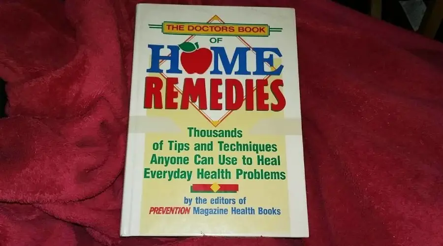 A book titled "The Doctors Book of Home Remedies" lies on a red fabric. The cover mentions "Thousands of Tips and Techniques Anyone Can Use to Heal Everyday Health Problems" by the editors of Prevention Magazine Health Books.