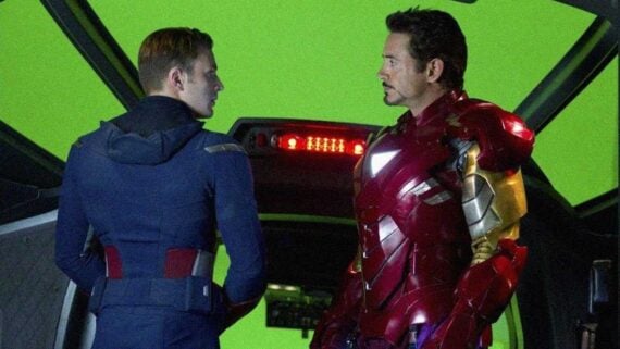 Chris Evans and Robert Downey Jr. standing on a superhero movie set in front of a large green screen during filming, showing the visual effects process behind Marvel movies.