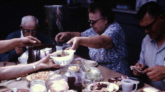Serious middle-class mom serving dinner to her family in a 1960s kitchen.
