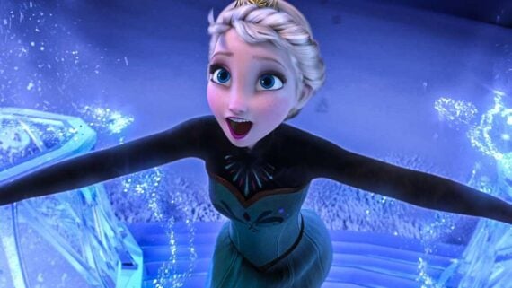Animated character Elsa from the movie "Frozen" stands with arms outstretched, looking excited and surrounded by icy, sparkling blue light and snow as if using her ice powers.