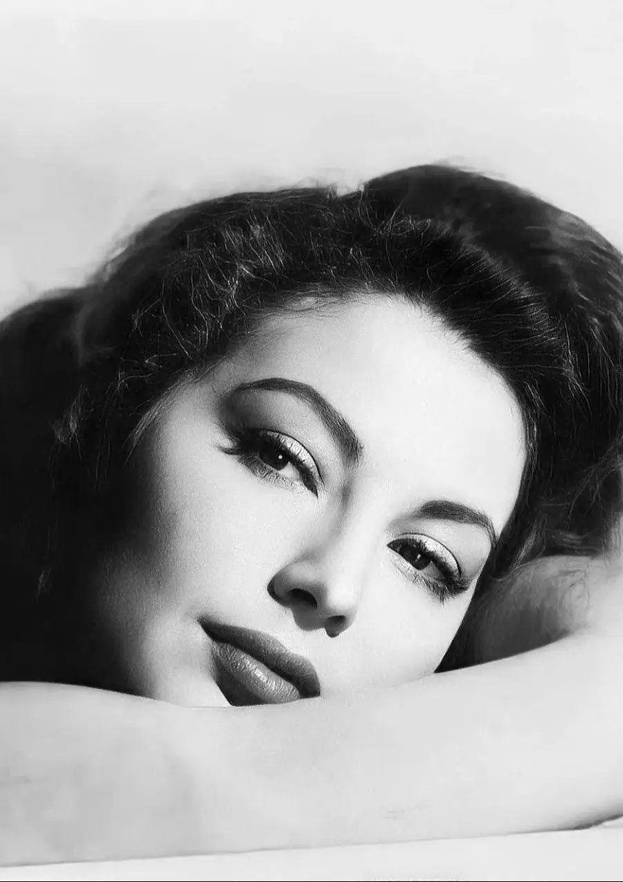 A black and white close-up portrait of a woman with wavy hair, resting her head on her arm, looking slightly upward with a serene expression.