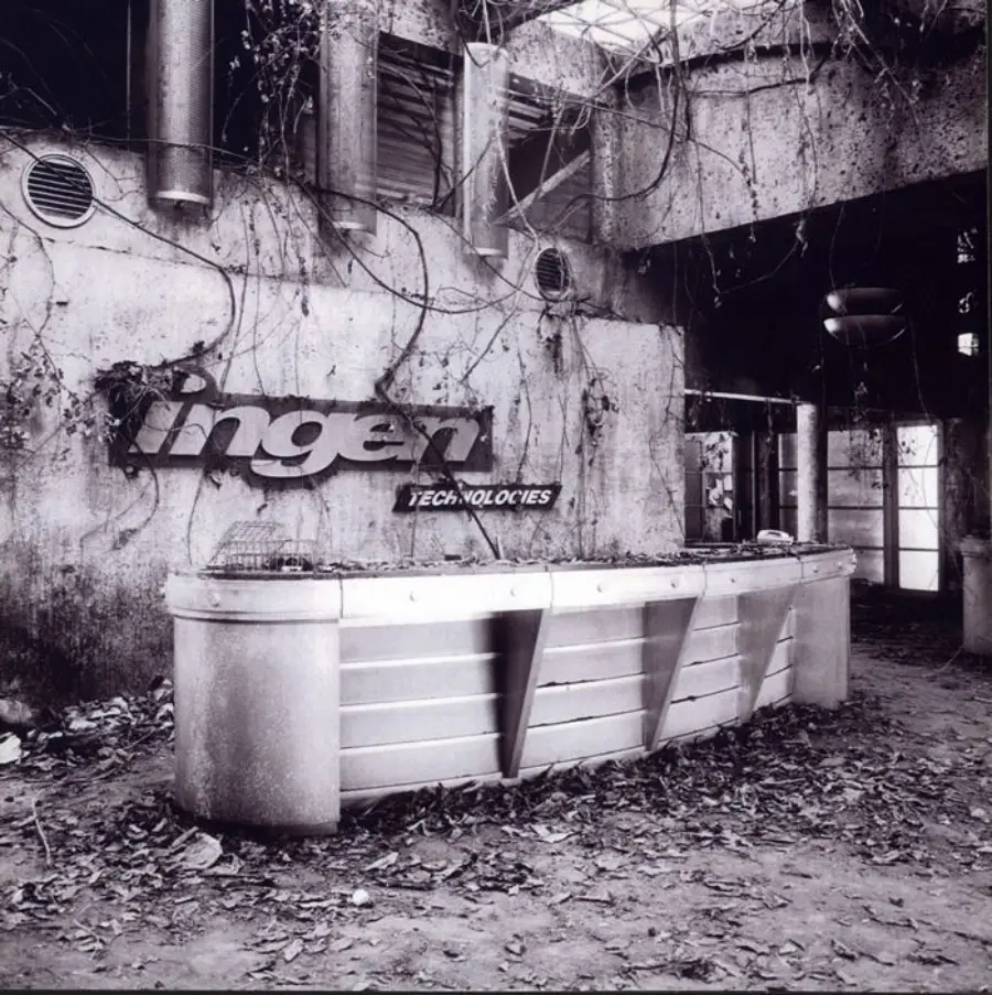 An abandoned, overgrown reception area with a damaged "InGen Technologies" sign on the wall and a metal front desk surrounded by fallen leaves and vines.