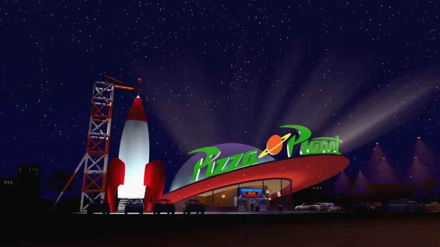 A night scene showing a brightly lit, futuristic pizza restaurant called "Pizza Planet" with a large rocket ship and neon sign, set against a starry sky. Cars are parked outside the building.
