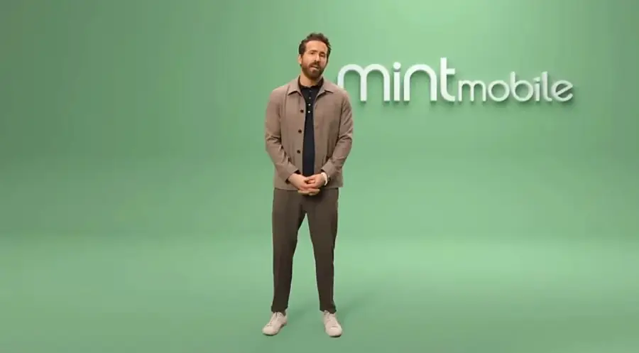 A man in casual clothing stands on a green background with the "mint mobile" logo displayed behind him.