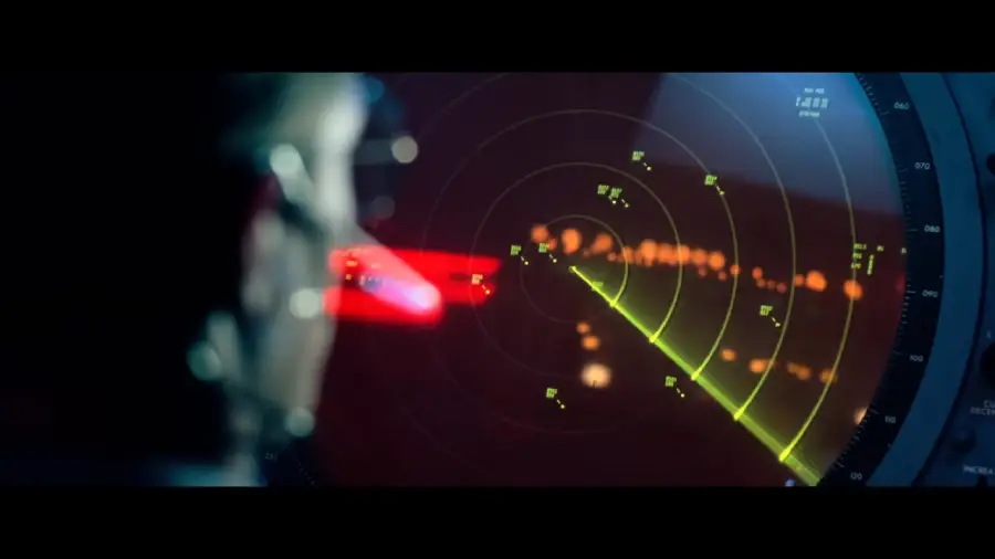 A person looks at a radar screen displaying green lines and glowing dots, indicating detected objects or targets, with a dark background and reflections of light.
