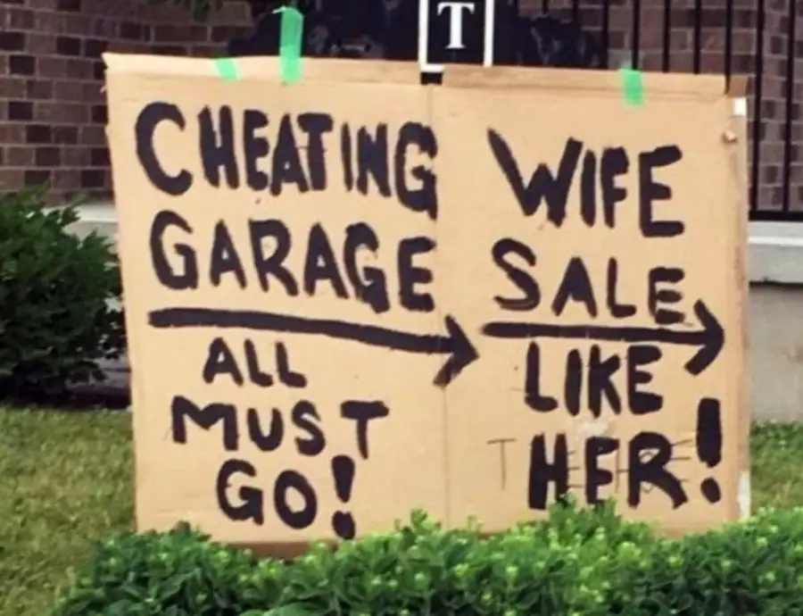 A cardboard sign in a yard reads, "CHEATING GARAGE ALL MUST GO! → WIFE SALE LIKE HER!" with large handwritten letters and arrows pointing right.