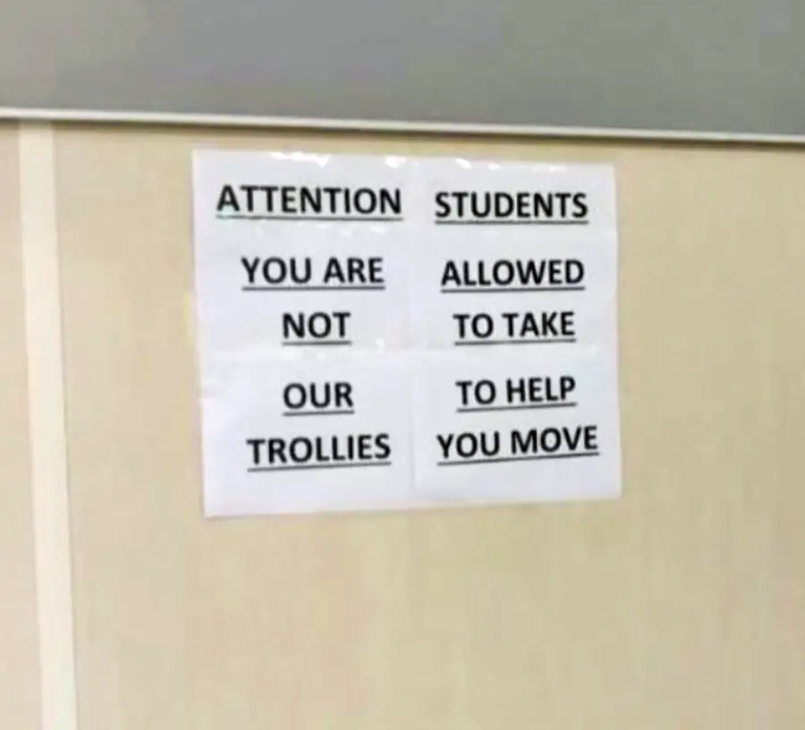 A sign on a wall reads: "ATTENTION STUDENTS YOU ARE NOT ALLOWED TO TAKE OUR TROLLIES TO HELP YOU MOVE." The message is printed on four sheets of white paper.