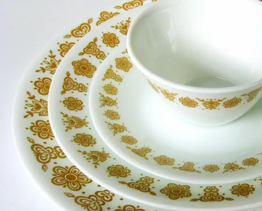 White vintage dishes, including a cup, saucer, and two plates, arranged in a stack. All pieces feature a yellow and brown floral pattern along the edges.