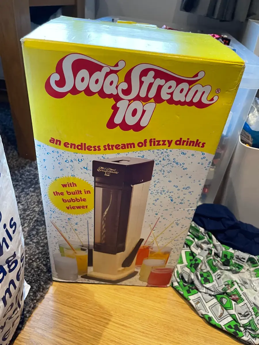 A SodaStream 101 box displays the soda maker with colorful fizzy drinks, bubbles, and the slogan "an endless stream of fizzy drinks" on the front. The packaging is mostly yellow and white with red text.