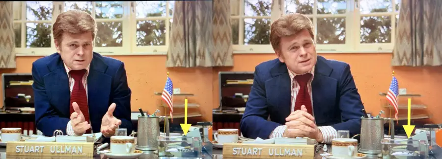 Two side-by-side images of a man in a suit sitting at a desk labeled "Stuart Ullman." On each desk, a yellow arrow points to a stack of papers near a cup and a small American flag. A window with curtains is in the background.