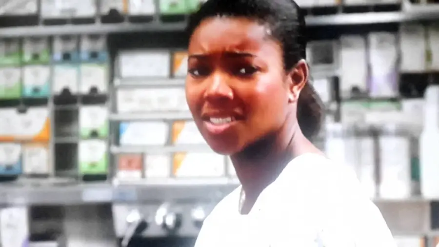 A woman wearing a white shirt stands in front of shelves filled with various boxes and medical supplies, looking slightly concerned or uncertain.