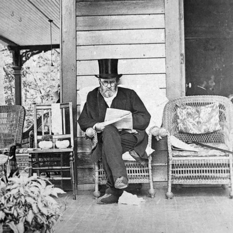 An older man wearing a top hat and glasses sits on a wicker chair on a porch, reading a newspaper. There are potted plants, a small table, and another empty wicker chair nearby.