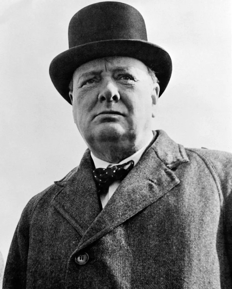 A black and white photo of an older man wearing a dark bowler hat, a bow tie, and a heavy coat, looking directly at the camera with a serious expression.