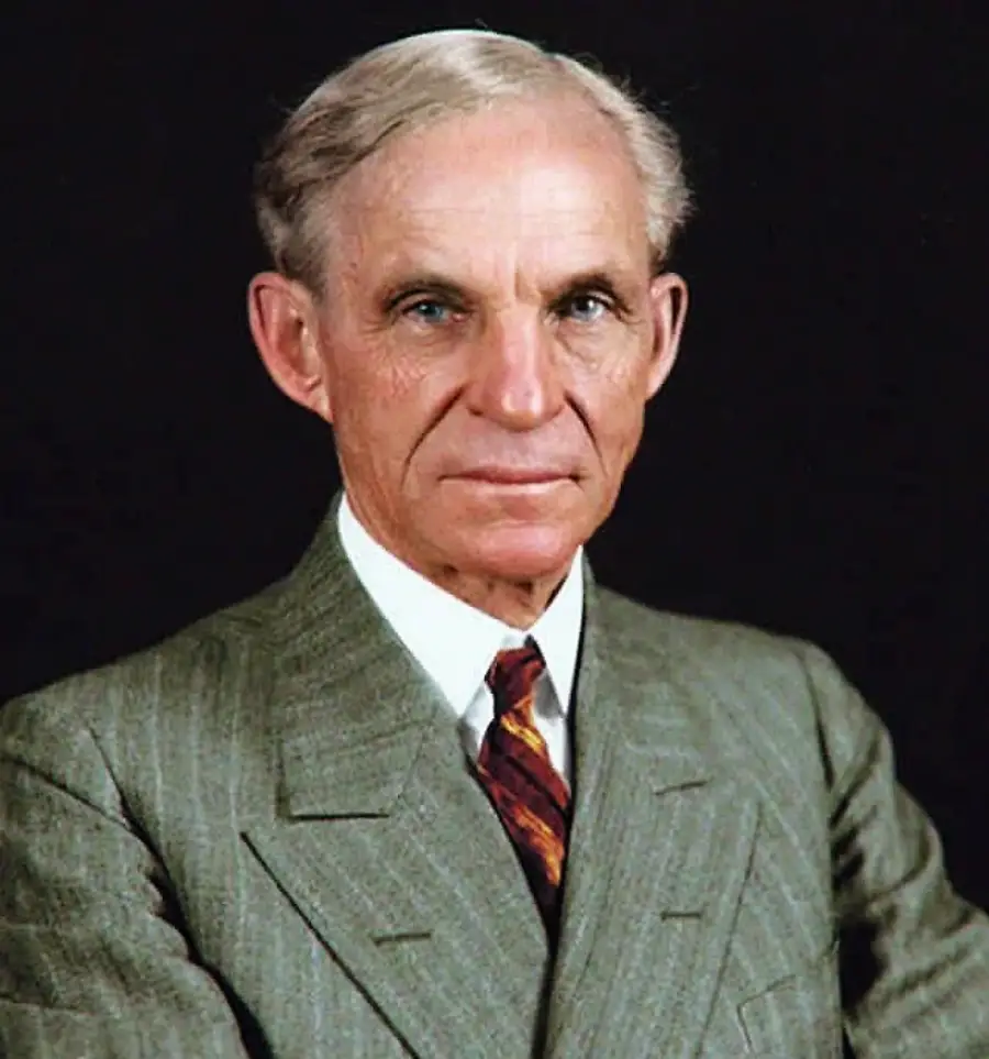 An older man with gray hair and blue eyes wearing a green pinstripe suit, white shirt, and patterned tie, posing against a dark background.