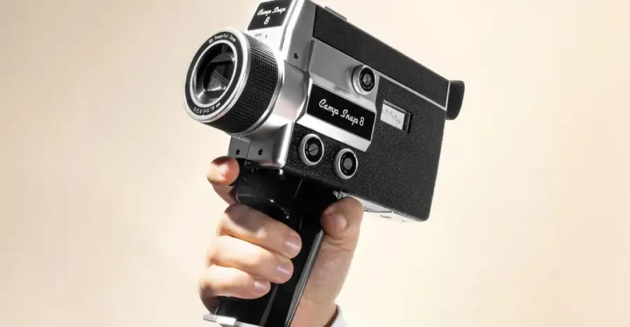 A person’s hand holding up a vintage black and silver Super 8 movie camera against a plain light background.
