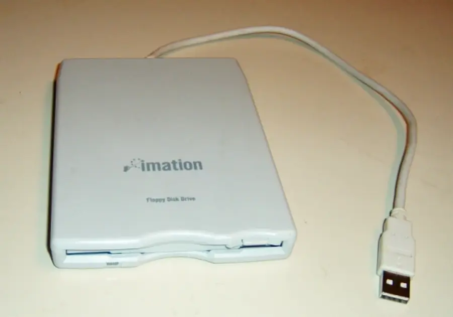 A white external Imation floppy disk drive with a USB cable attached, placed on a light-colored surface. The drive’s front slot for inserting floppy disks is visible.