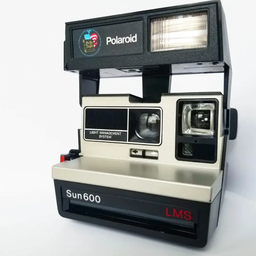 A vintage Polaroid Sun 600 LMS instant camera with a black and silver body, flash at the top, and "Polaroid" and "Sun 600 LMS" labels, photographed against a white background.
