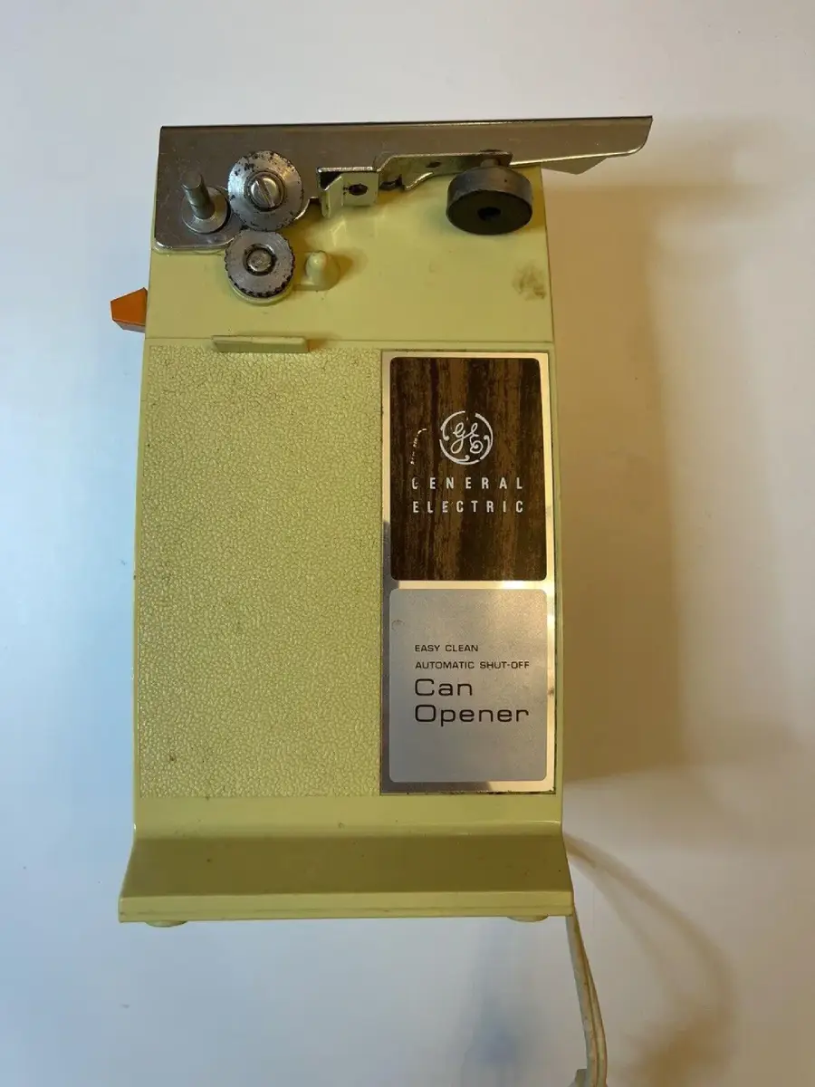 A vintage yellow General Electric electric can opener with metal gears, an easy-clean label, and a power cord, viewed from above on a white background.