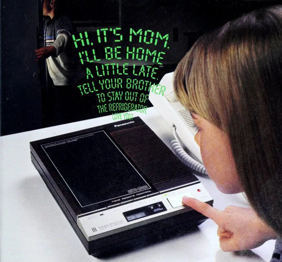 A girl listens to a message on a vintage cassette answering machine, with green text above reading, "Hi, it's Mom. I'll be home a little late. Tell your brother to stay out of the refrigerator. Love you!