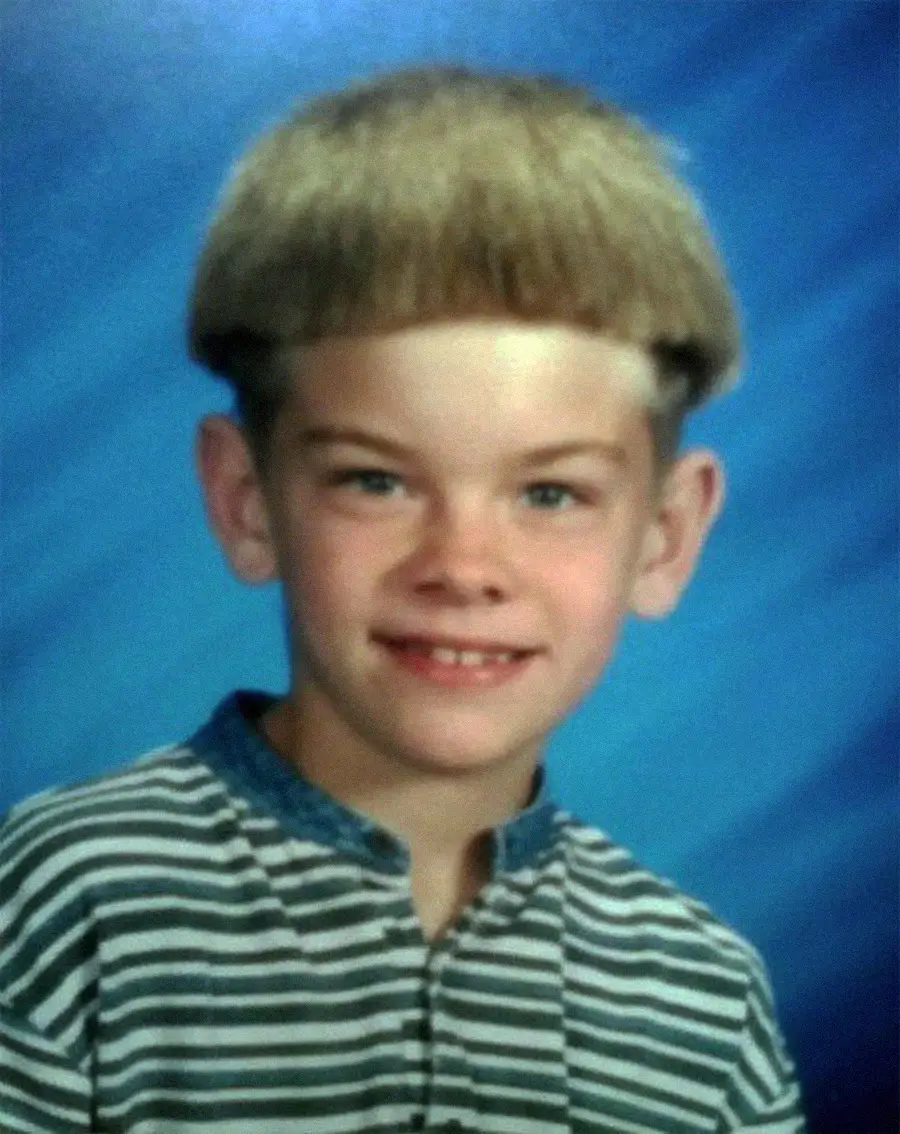 A young boy with light skin and a bowl haircut smiles at the camera. He is wearing a striped shirt with a blue collar. The background is a blue gradient, typical of school portrait photos.