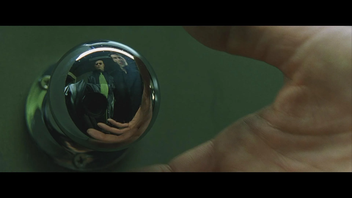 A close-up of a shiny doorknob reflecting two people, with a hand reaching toward it. The reflection is slightly distorted, showing their faces and upper bodies against a green background.