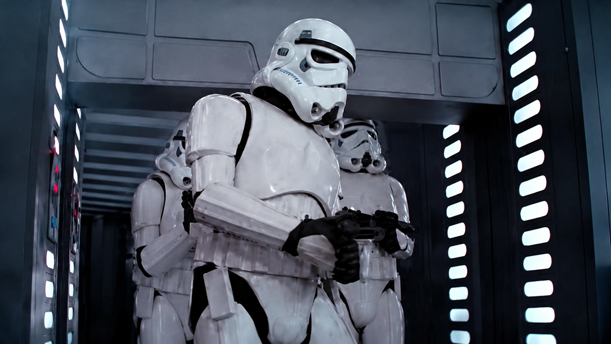 A group of Stormtroopers in white armor and helmets stand in formation inside a metallic, futuristic hallway with bright vertical lights along the walls.