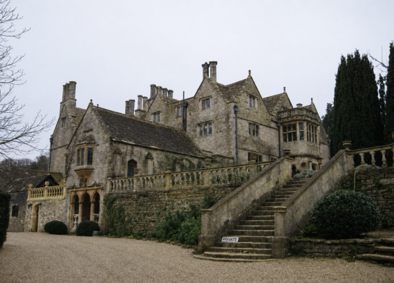 Large stone manor house with multiple chimneys, gabled roofs, and bay windows. Stone steps lead up to the entrance, with a "Private" sign at the bottom. Surrounded by a gravel driveway and tall greenery. Radiohead Ok Computer. Music. Record. Album.