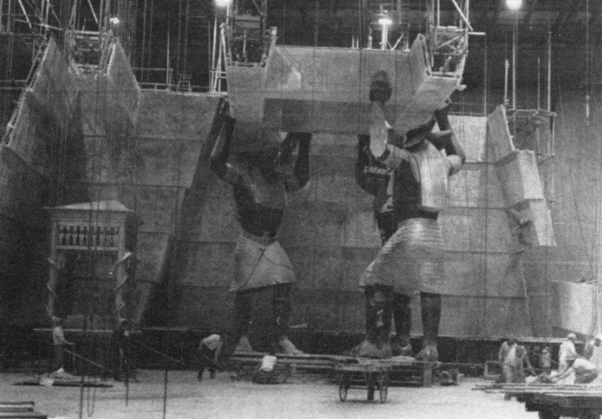 Two workers assemble a large set piece depicting two armored figures holding up a stone structure, with scaffolding and building materials visible in a spacious indoor studio. 5. Raiders of the Lost Ark’s Well of Souls