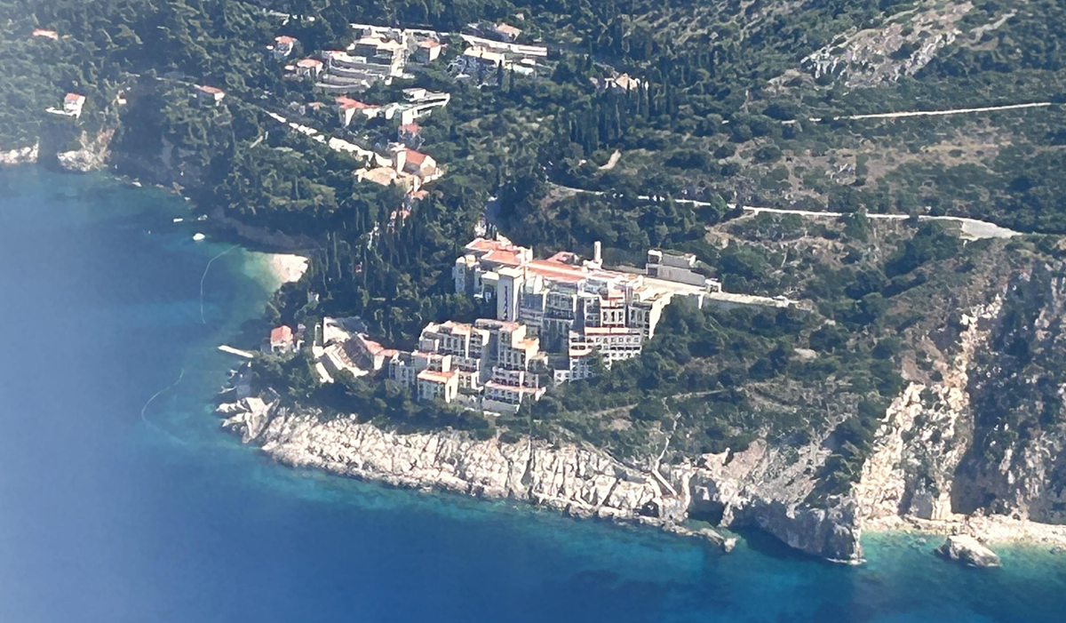 Aerial view of a large coastal monastery complex with multiple buildings on a forested hillside, surrounded by turquoise waters and rocky cliffs, with other smaller structures scattered nearby. 1. Hotel Belvedere, Dubrovnik, Croatia