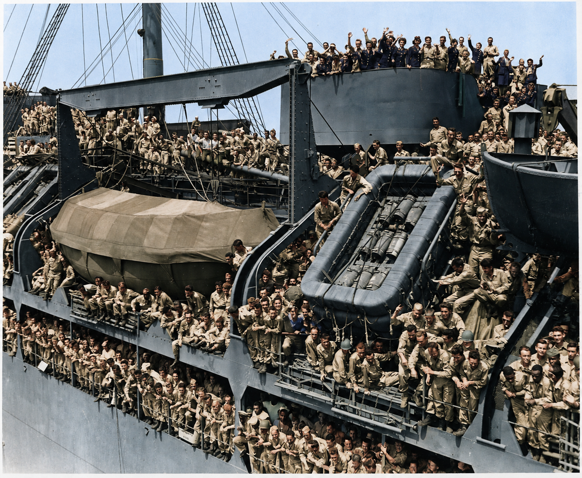 A large group of soldiers in uniform crowd the decks and railings of a military ship, many smiling and waving at the camera, suggesting a scene of celebration or homecoming.