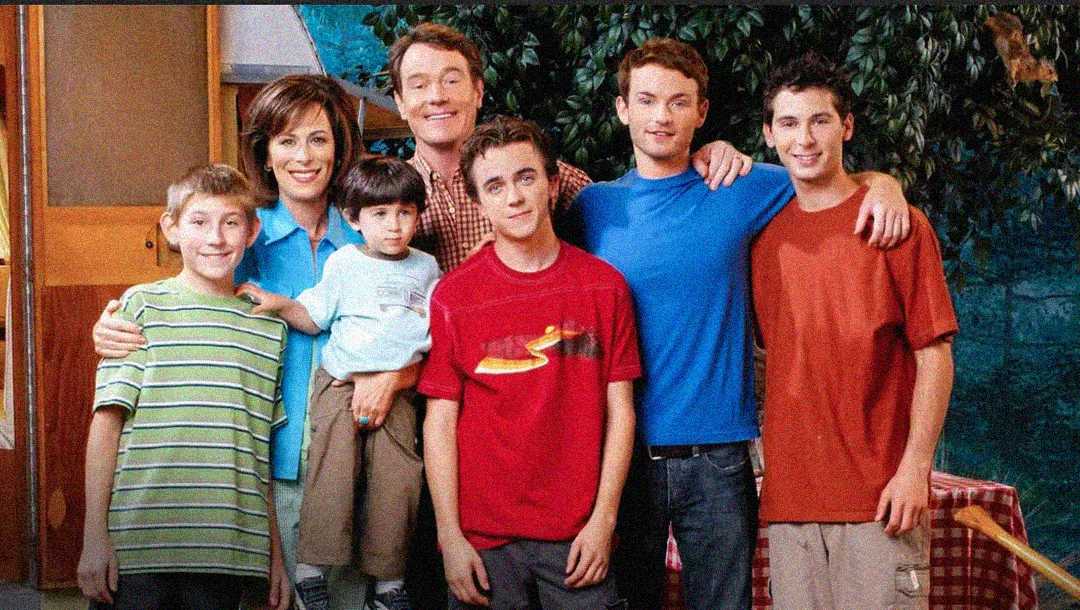 A family of seven poses together, smiling. The father and mother stand in the back with their arms around their five sons, who stand in front, wearing casual clothes in various colors.