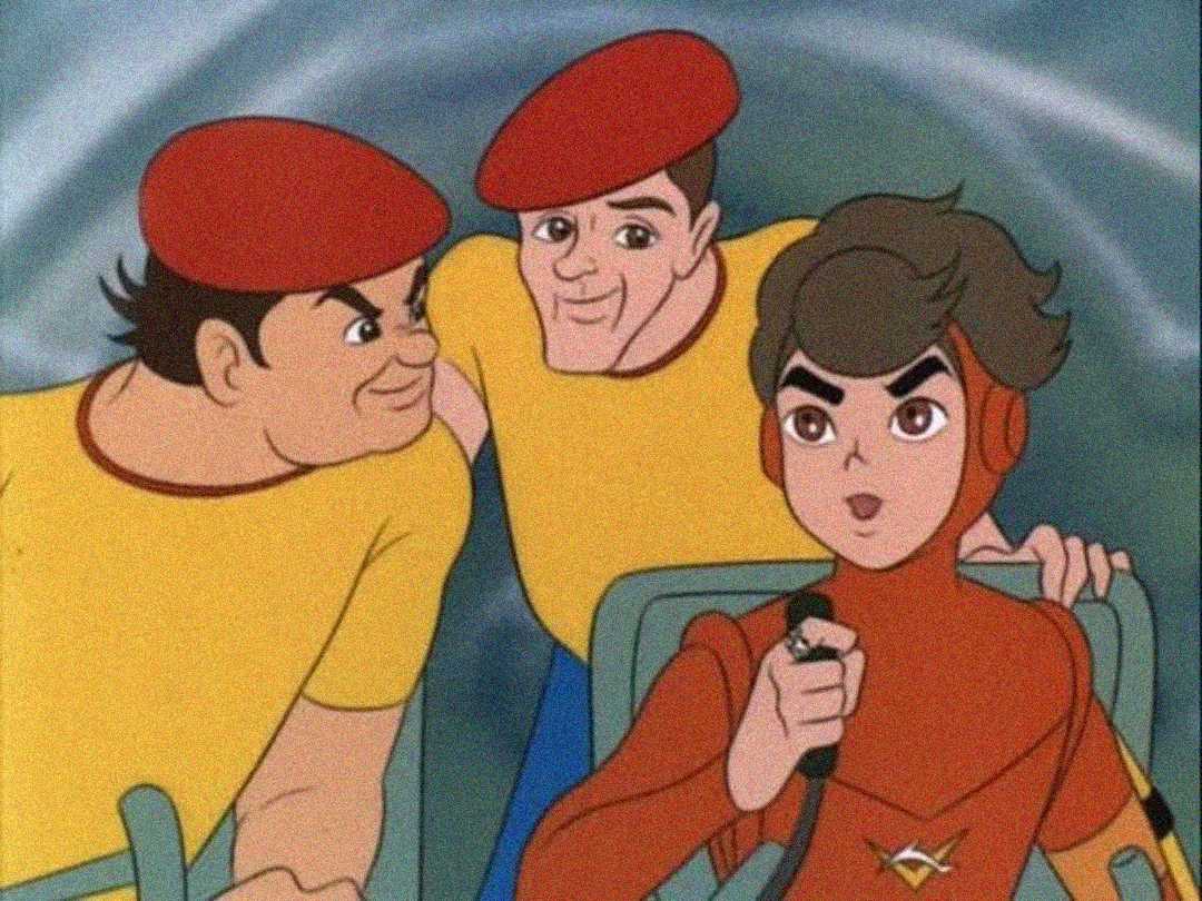 Three animated characters are shown: two men in yellow shirts and red berets looking at a young person in a red suit and headset who is sitting and holding a control lever, possibly piloting a vehicle.
