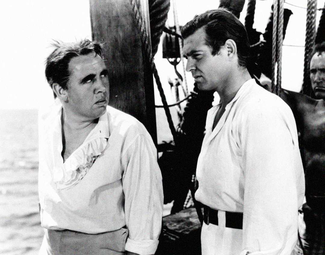 Two men in old-fashioned sailor shirts stand on the deck of a ship, looking at each other with serious expressions. One man has tousled hair and a ruffled collar, while the other wears a belted shirt.