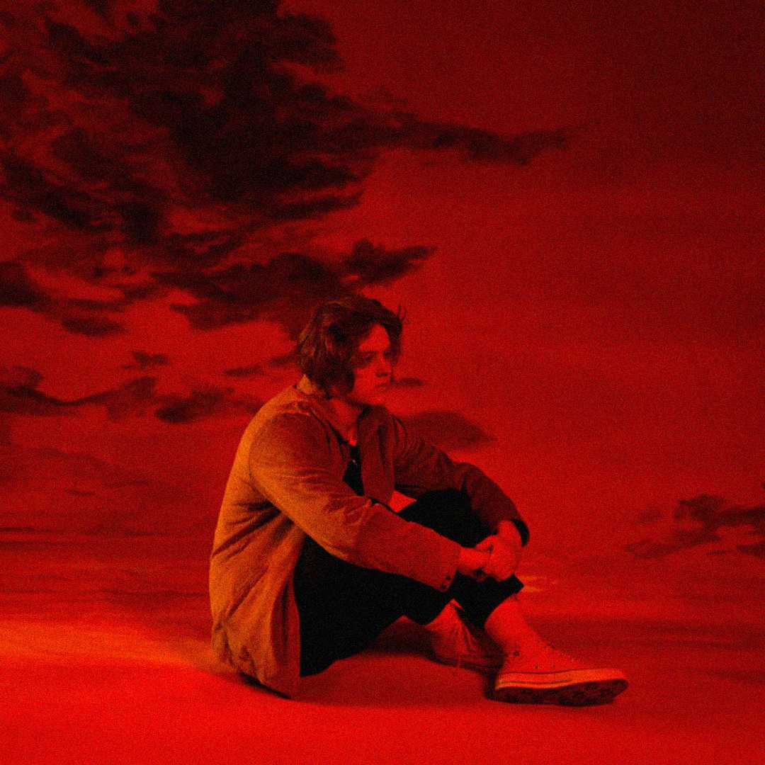 A person with medium-length hair sits on the ground with arms resting on their knees, surrounded by a deep red background and shadowy clouds, creating a moody, dramatic atmosphere.